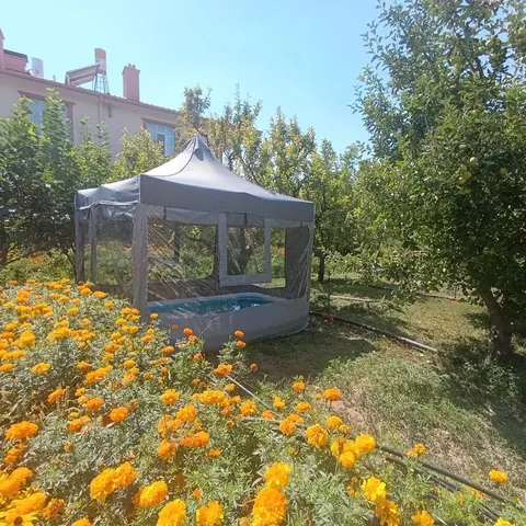 Çiçekli bahçede şeffaf pencereli gazebo çadır